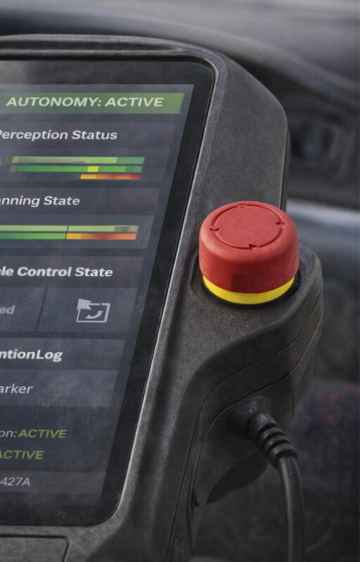 Close-up of a teach pendant with a touchscreen interface and a side-mounted red emergency stop button.