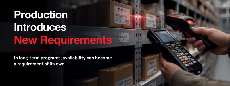 Warehouse shelves filled with boxed components as an operator uses a handheld barcode scanner to verify inventory for production planning.